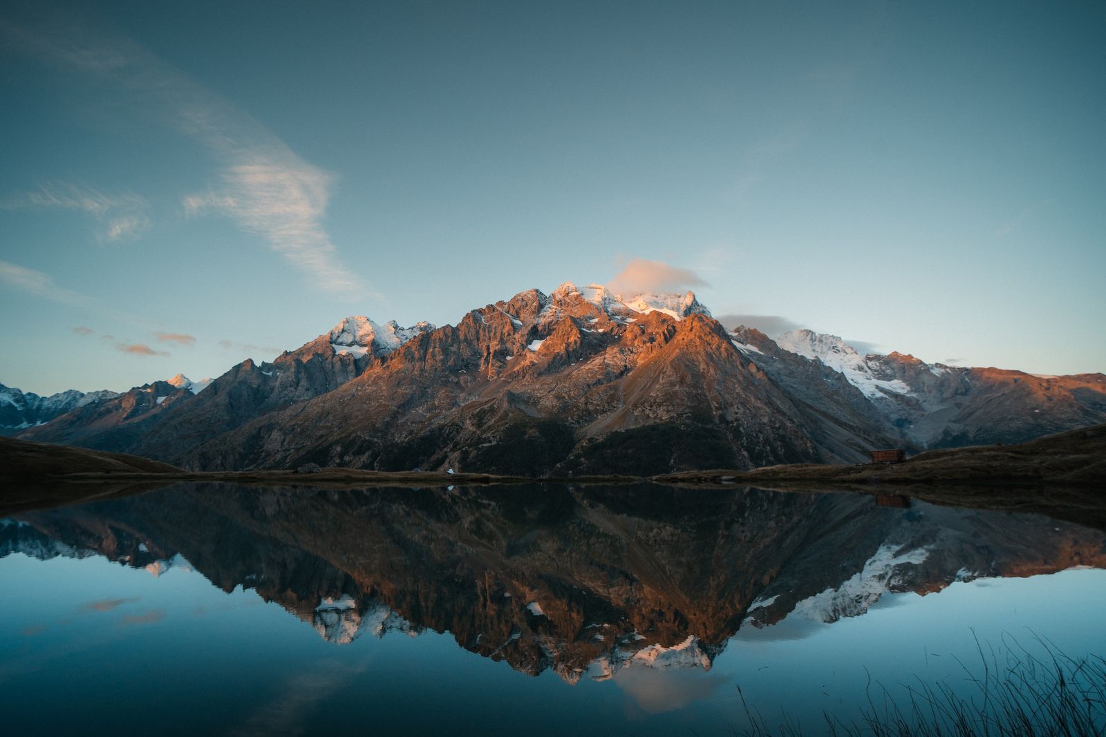 Snow-covered alpine mountains reflected in a still lake beneath a soft evening sky